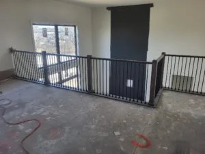 Loft edge guardrail with vertical black metal balusters and corner newel posts, unfinished floor