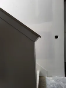 Painted stairwell knee wall with a wood cap and mitered return along the top edge