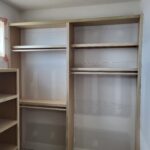 Raw wood closet shelving and hanging rod units installed in unfinished state, ready for paint.