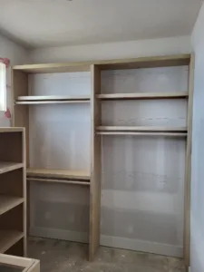Raw wood shelving and hanging rod units installed on both walls, unfinished, ready for paint.