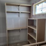 Unfinished closet shelving with multiple tiers, metal support brackets, and hanging rod—ready for paint.