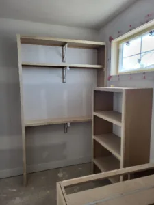 Unfinished closet shelving with an angled shelf near a window and an open cubby unit below, raw wood.