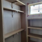 Raw wood closet shelving with hanging rods and metal support brackets, pre-paint stage.