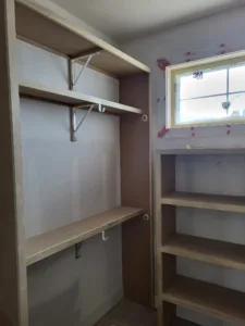 Raw wood closet shelves mounted on metal L-brackets near a window, unfinished stage.