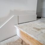 Primed baseboard installed at wall-to-floor junction on subfloor; raw wood trim ready for paint.