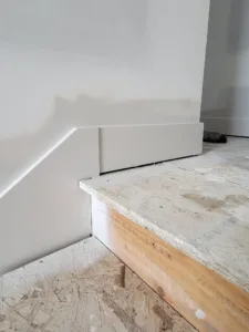 Primed white baseboard installed along a stair stringer down to subfloor, ready for paint
