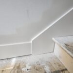 Painted white baseboard installed at wall-floor junction on subfloor, ready for flooring install.