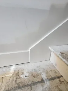 Painted white baseboard installed along a stair stringer down to subfloor, ready for flooring