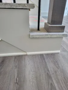Painted baseboard and shoe molding meeting wood-look flooring at a stair transition