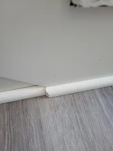 Painted baseboard and shoe molding installed at a wall-floor junction with wood-look flooring