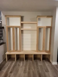 Built-in mudroom locker with raw wood side cabinets, open cubby bench, and center panel, unfinished.