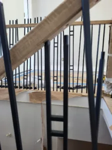 Closeup of vertical black metal balusters being installed into a wood cap rail, unfinished