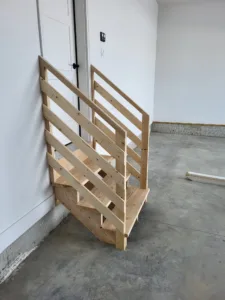 Completed wood garage steps with horizontal slat railing, unfinished wood, positioned near entry door.