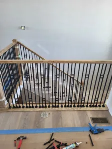 Overhead view of stairwell opening during metal baluster installation, tools on taped subfloor