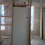 Primed apartment unit entry door slab installed in wood frame with casing, ready for paint.
