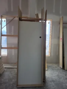 Primed slab door standing in a wood-framed room with exposed studs and a window opening.