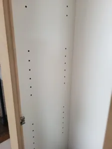 Cabinet side panel interior with painted white finish and a row of pre-drilled shelf pin holes.