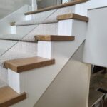 Finished stair installation with wood treads, nosing, handrail, and painted white risers and skirt board.