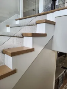 Finished stair with carpet treads, wood nosing caps, glass railing, and painted white risers
