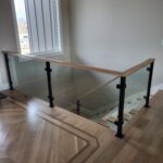 Completed horizontal-rod glass railing with black metal posts and wood cap rail, modern style.
