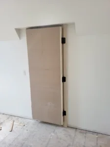 Unfinished wood pocket door slab slid partly into wall pocket, roller hardware visible at top.