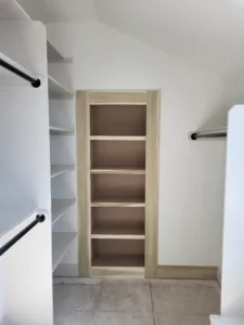 Tall natural wood closet shelf tower with five shelves beside a hanging rod, under a sloped ceiling.