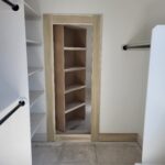 Walk-in closet cased opening with natural wood jamb and casing, shelving and rods installed, ready for paint.