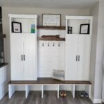 Custom mudroom locker with painted white cabinetry, open cubby bench seating, upper storage cabinets, and decorative wood shelving with hooks.