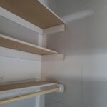 Closet shelving with particle-board shelves, white brackets, and wooden hanging rod installed.