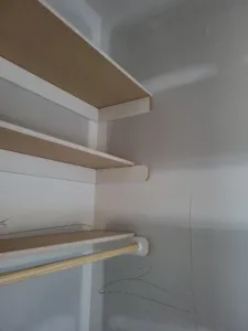 Angled particleboard closet shelves on wood cleats above a hanging rod, unfinished raw wood.