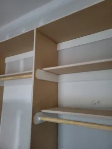 White painted closet shelves with a wood hanging rod and textured backing board, multi-tier.