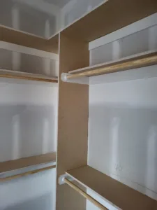 Closet interior with raw wood shelves and a wood hanging rod, unpainted trim stage.