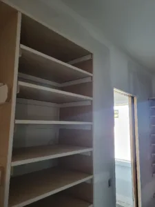 Multi-tier particleboard closet shelving under a sloped ceiling, unfinished raw wood.