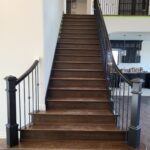 Completed stair railing with black newel posts, horizontal rod balusters, and curved handrail with rail fittings.