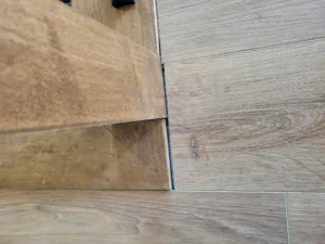 Stained wood trim piece with a mitered corner return, set beside wood-look tile flooring