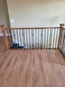 Stained wood newel posts and handrail with vertical black metal balusters at a stair landing