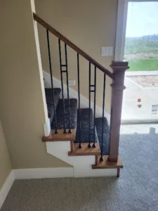 Staircase with dark wood newel post, wood handrail, vertical iron balusters, and carpet treads