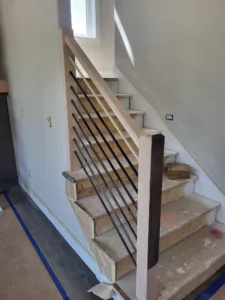 Wood framed stair opening with thin diagonal wire rail elements and a dark wood newel post
