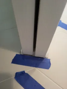 Painted door jamb and casing corner with blue painter's tape at the base, meeting tile flooring.