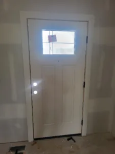 Painted white single exterior door with square transom window above, hardware not yet installed