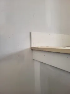 Painted closet shelf with bullnose edge and visible fastener holes before final touch-up.
