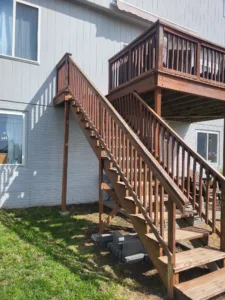 Stained wood exterior deck with a stairway, railings, and balusters descending to the yard