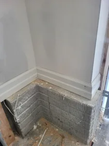 Painted white baseboard installed at an inside wall corner above exposed concrete block foundation.