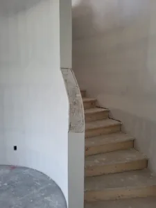 Notched skirt board on a curved staircase, raw wood treads, drywall walls ready for paint.