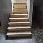 Stair risers and treads with finished white skirt boards and handrail installed, raw wood awaiting paint.