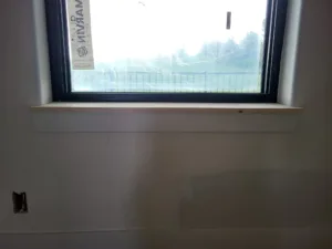 Finished wood sill installed below a black framed window, trees visible through the glass.