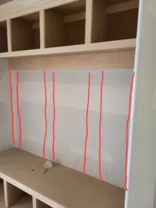Built-in cubby unit under construction with raw plywood compartments and layout tape marking stud locations.