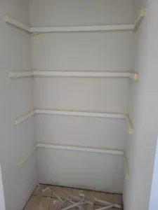 Four white hanging rods mounted on wall brackets in a wraparound closet corner, unfinished stage.