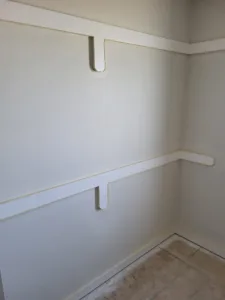 Painted wood shelf cleats installed along two closet walls, ready for shelf boards to be added