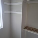 Closet shelving installation in progress with two horizontal shelves and vertical divider, trim materials staged nearby.
